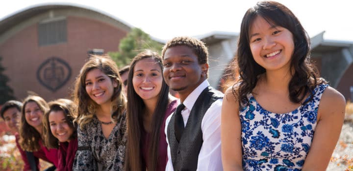 A group of First Scholar program students pose outside with the Field House in the background.
