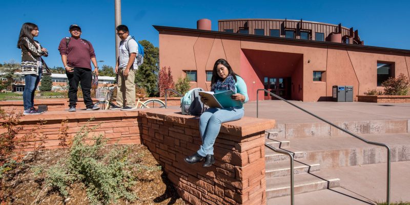 An NAU native students sits on a wall studying in front of the NACC.