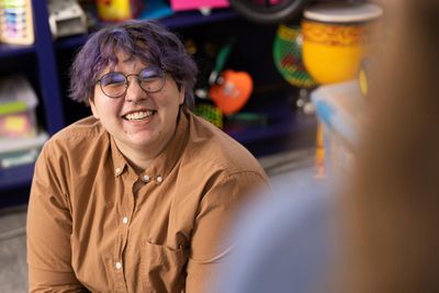 A student teacher sits on the floor of a classroom and smiles for the camera.