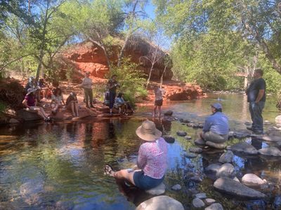 People sitting around a creek with red rocks around them