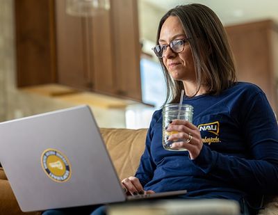 Woman sitting with a computer on her lap and a glass of water in her hand