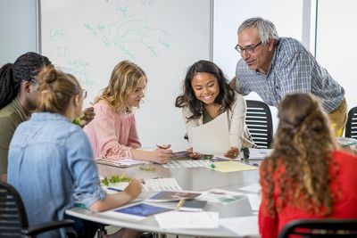 A group of students collaborate at a desk with their professor.