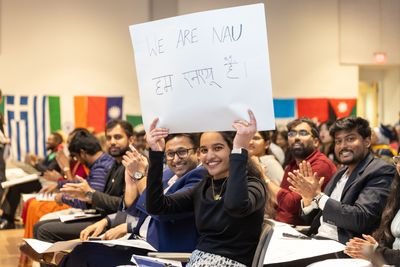 NAU international students smile while holding a sign that says "We are NAU" in both English and Hindi.