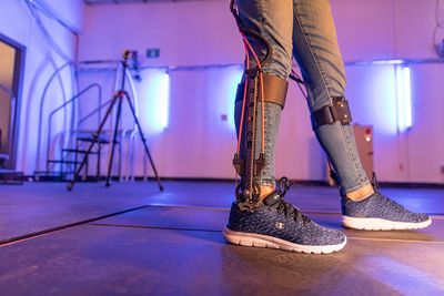 Person's legs and feet wearing casual clothing and sneakers, standing on a tiled floor in a room with neon lighting.