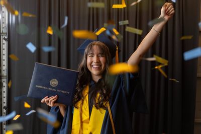 An NAU graduate smiles with excitement while holding their degree.