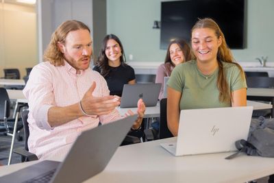 Professor sits with students and discusses psychology in front of laptop.
