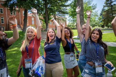 A group of new students excitedly raising their hands in front of Old Main at the NAU Flagstaff campus.