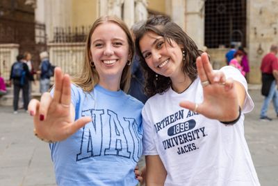 Two student are smiling for the camera and holding up the Jacks hand sign.
