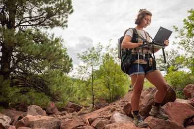 Student working on research in a red rock formation surrounded by trees.