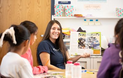 A College of Education student reads a picture book to a small group of young children in a classroom setting.