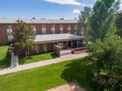 The exterior of Allen Hall, a residential living space, shaded by trees on a sunny day at NAU Flagstaff mountain campus.