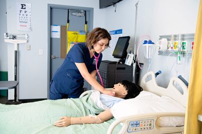 A nursing student uses a stethoscope to practice listening to heartbeats on a patient simulator.