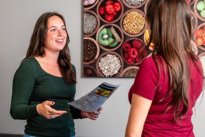 A student in the Nutrition program holds a pamphlet in front of a photograph with assorted fruits and healthy foods.
