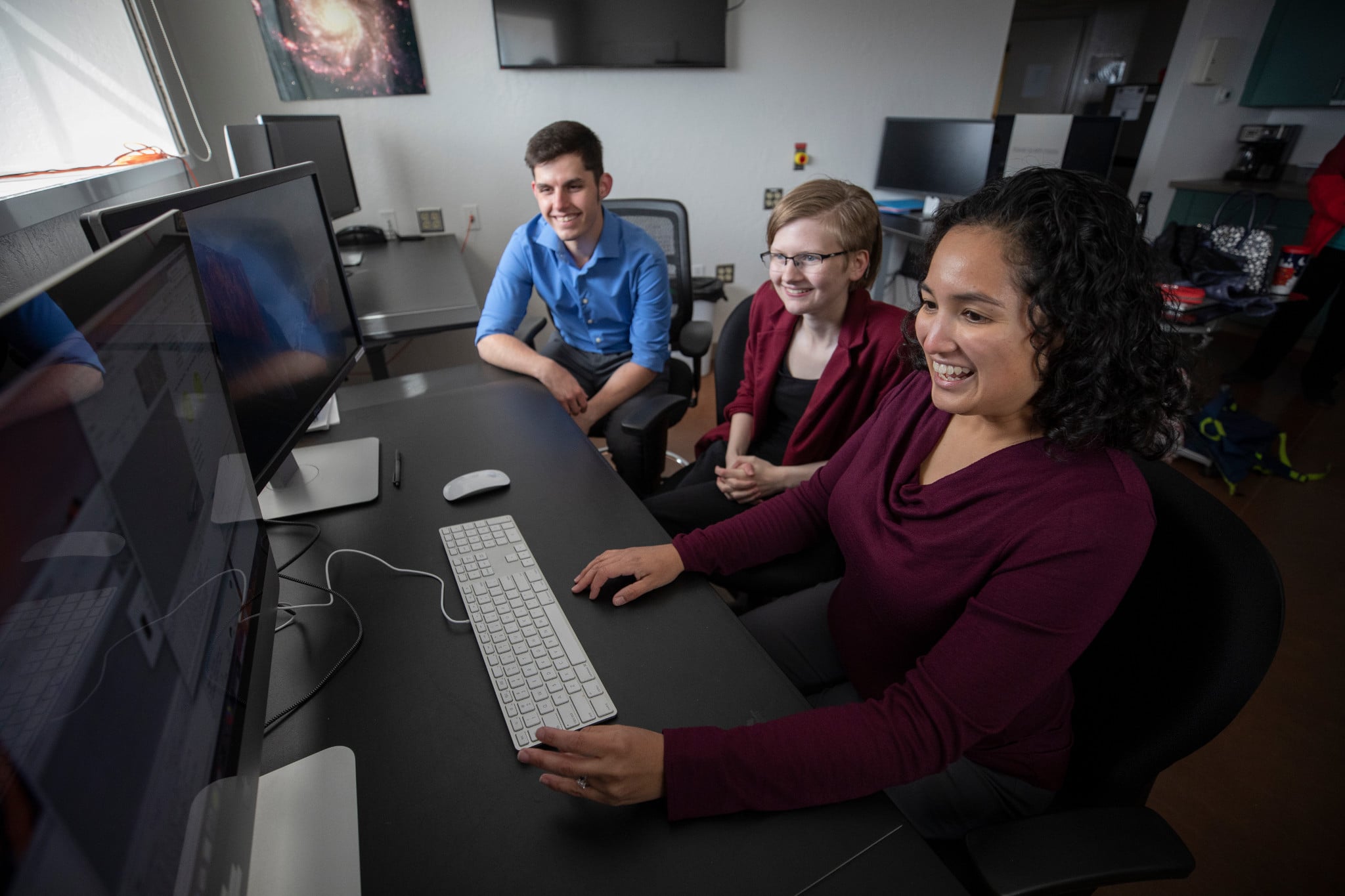 Three students sitting in front of several computer screens