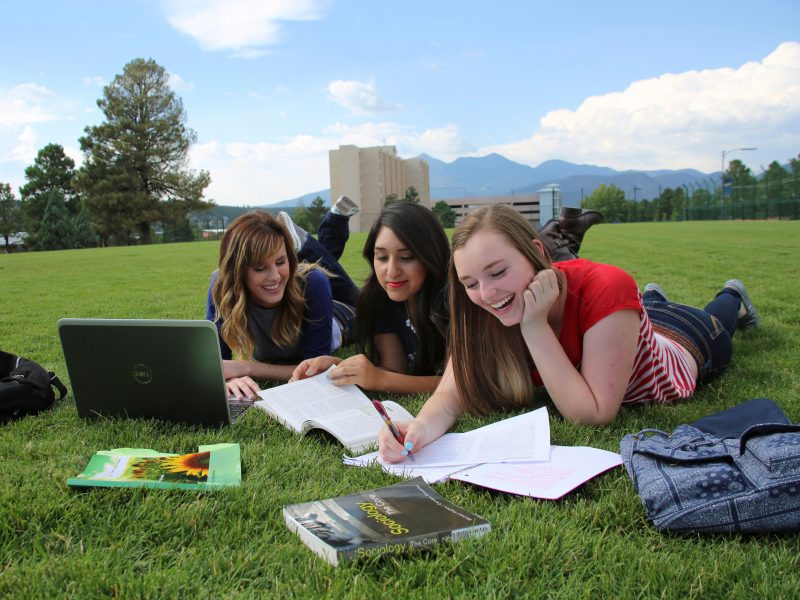 Three students studying together on a field on campus.