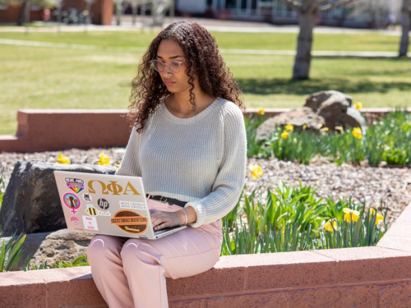 Student working on her laptop outside on a sunny day at Flagstaff campus.