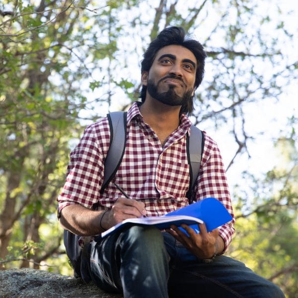 Student sits on a rock holding a notebook.