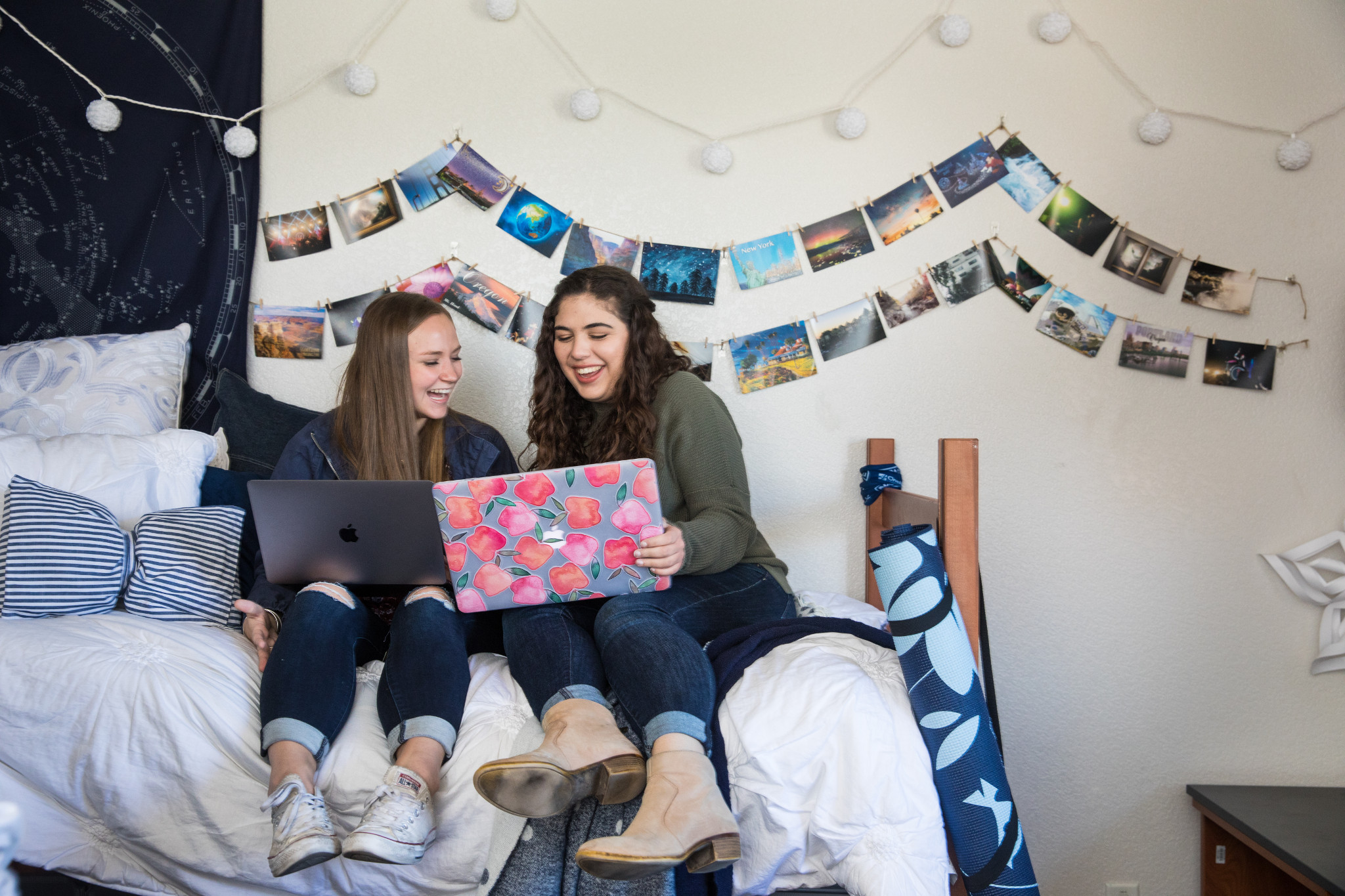 Students in dorm room laugh while studying on laptops.