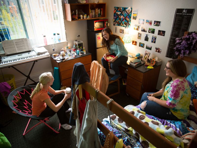 Students laugh while hanging out in dorm room.