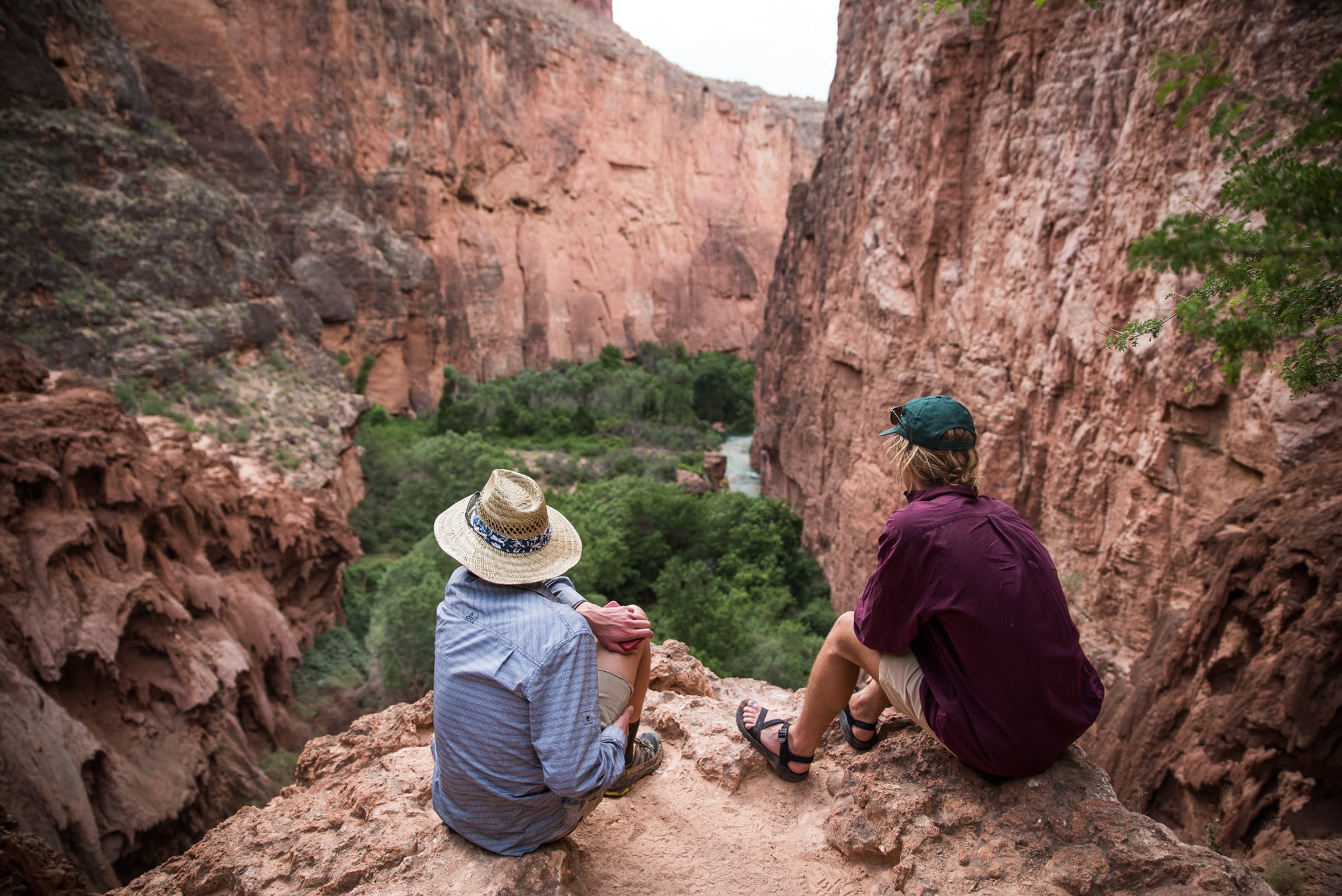 Two people sit on rock overlooking a canyon.