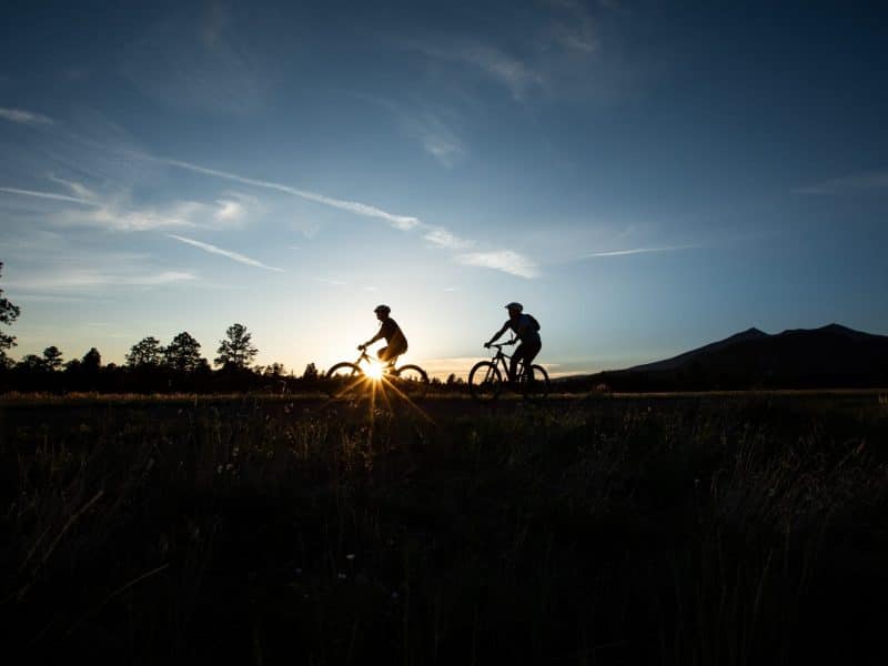 People ride bikes on the horizon as the sun rises.