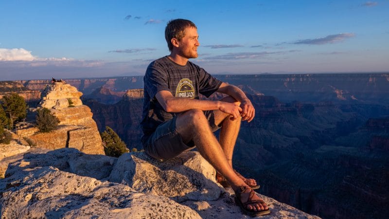 Student sits on large rock overlooking the Grand Canyon.