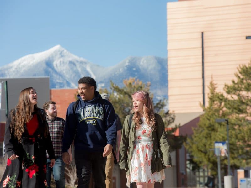 Students walk together on NAU campus in front of a snowy mountain peak.