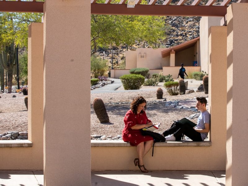 Two students sit on bench outside.