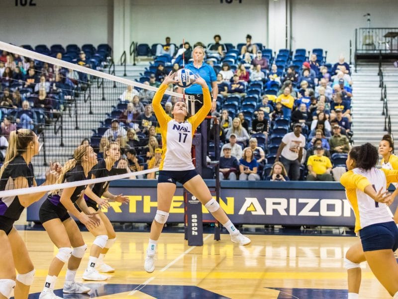 NAU volleyball player jumps in front of net to hit the ball.