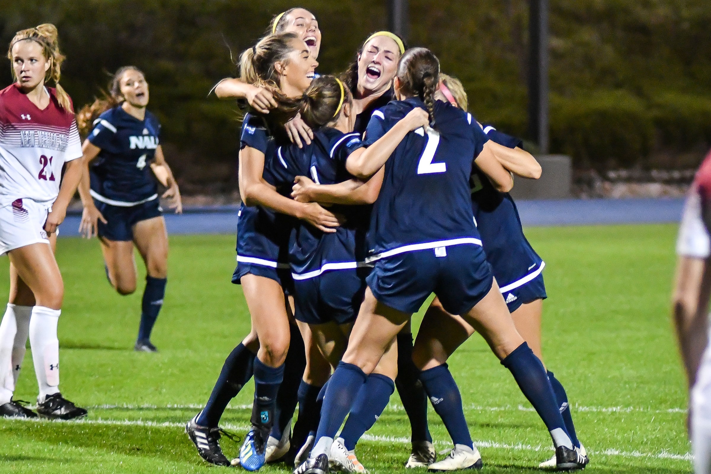 NAU soccer players excitingly hug each other on field.