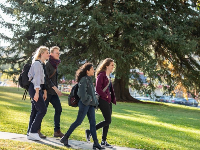 Four students walking together through campus in fall.