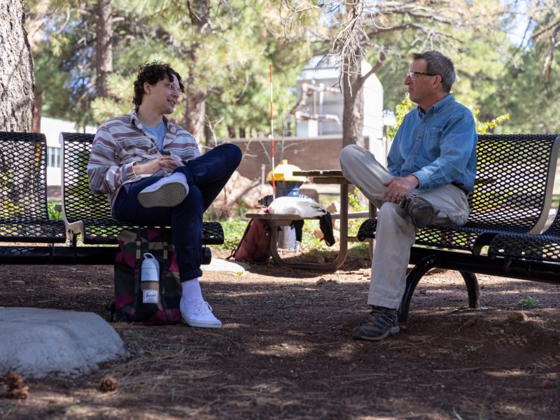 Student and professor talking outside on the bench at Flagstaff Mountain campus.