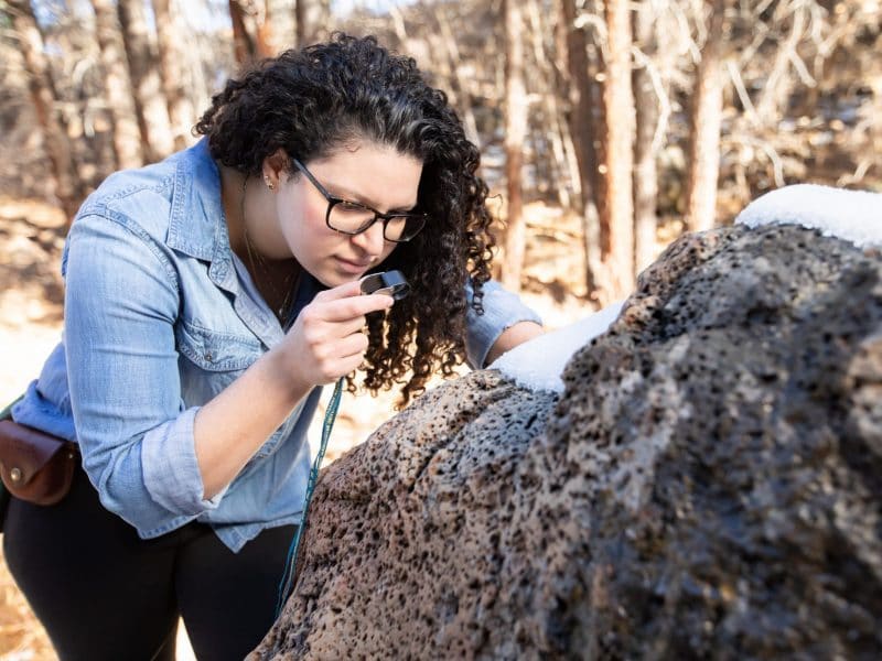 Geology student examines a boulder with a magnifying glass.
