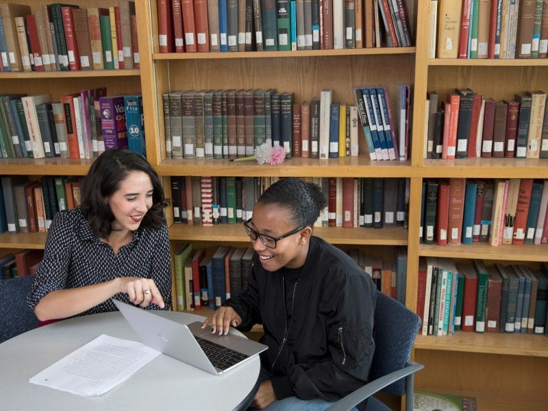 Professor and student smiling and working together in library