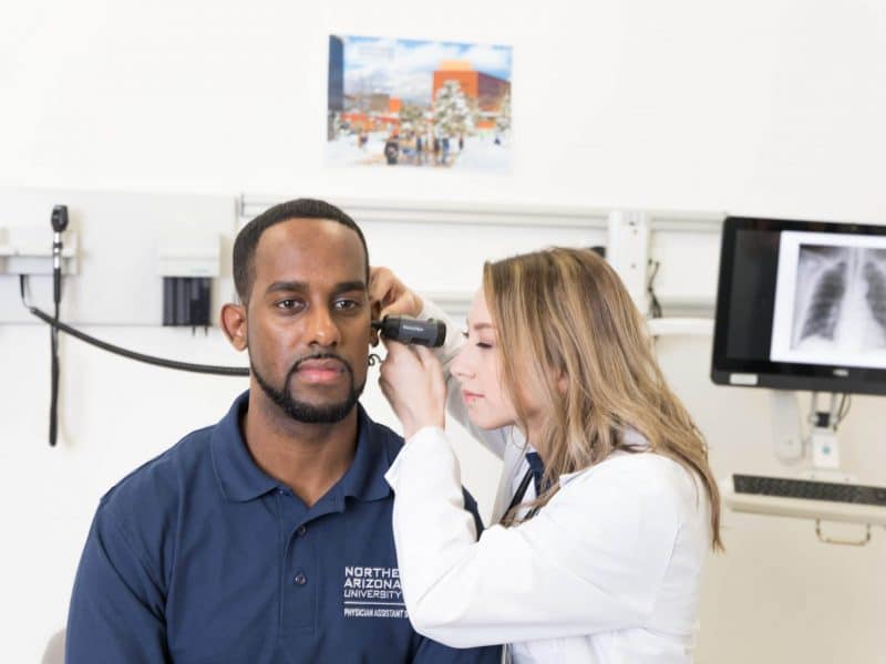 Physician assistant performs ear exam with otoscope.