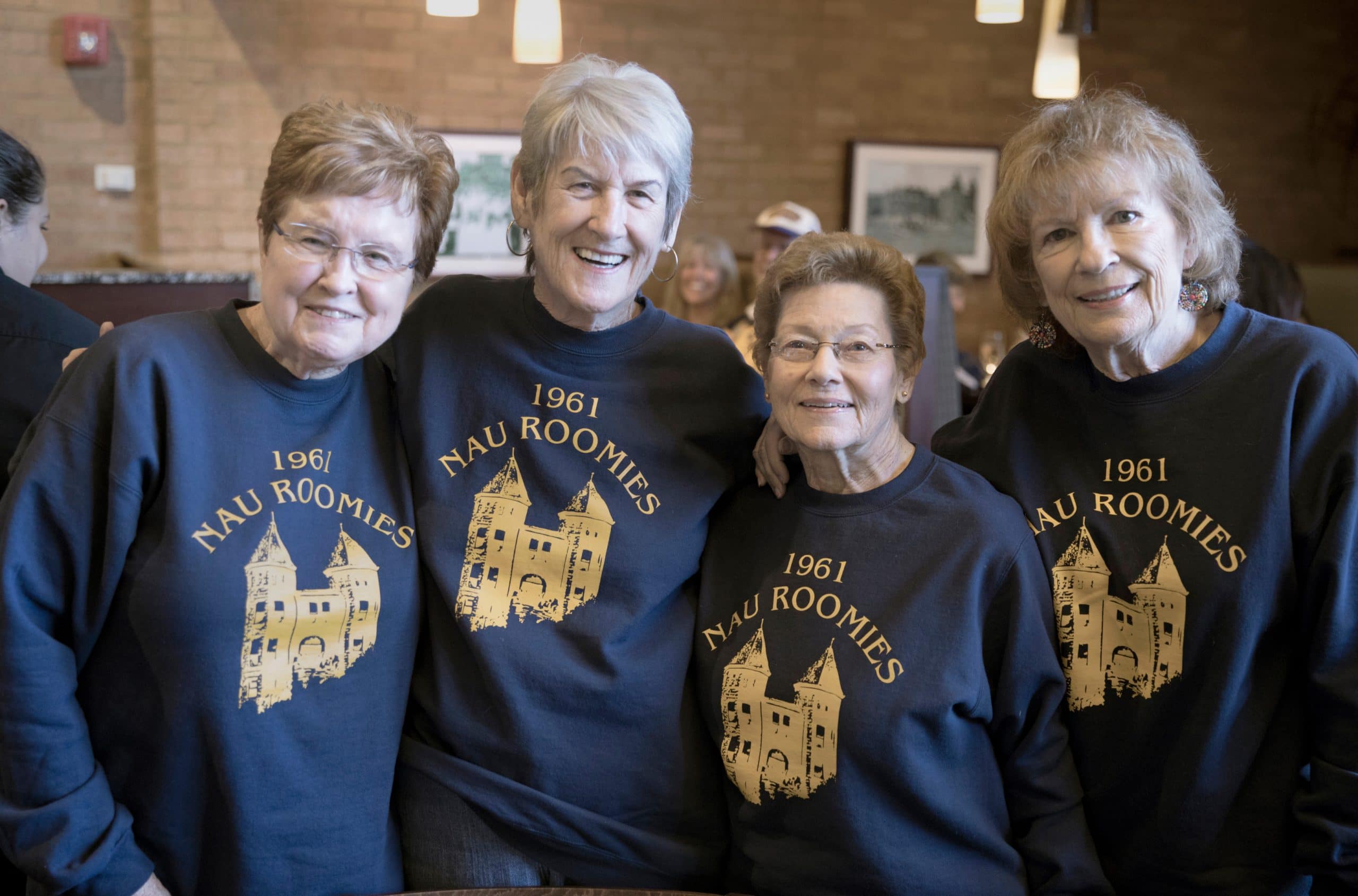 Alumni stand together wearing matching 1961 NAU roomies shirts.