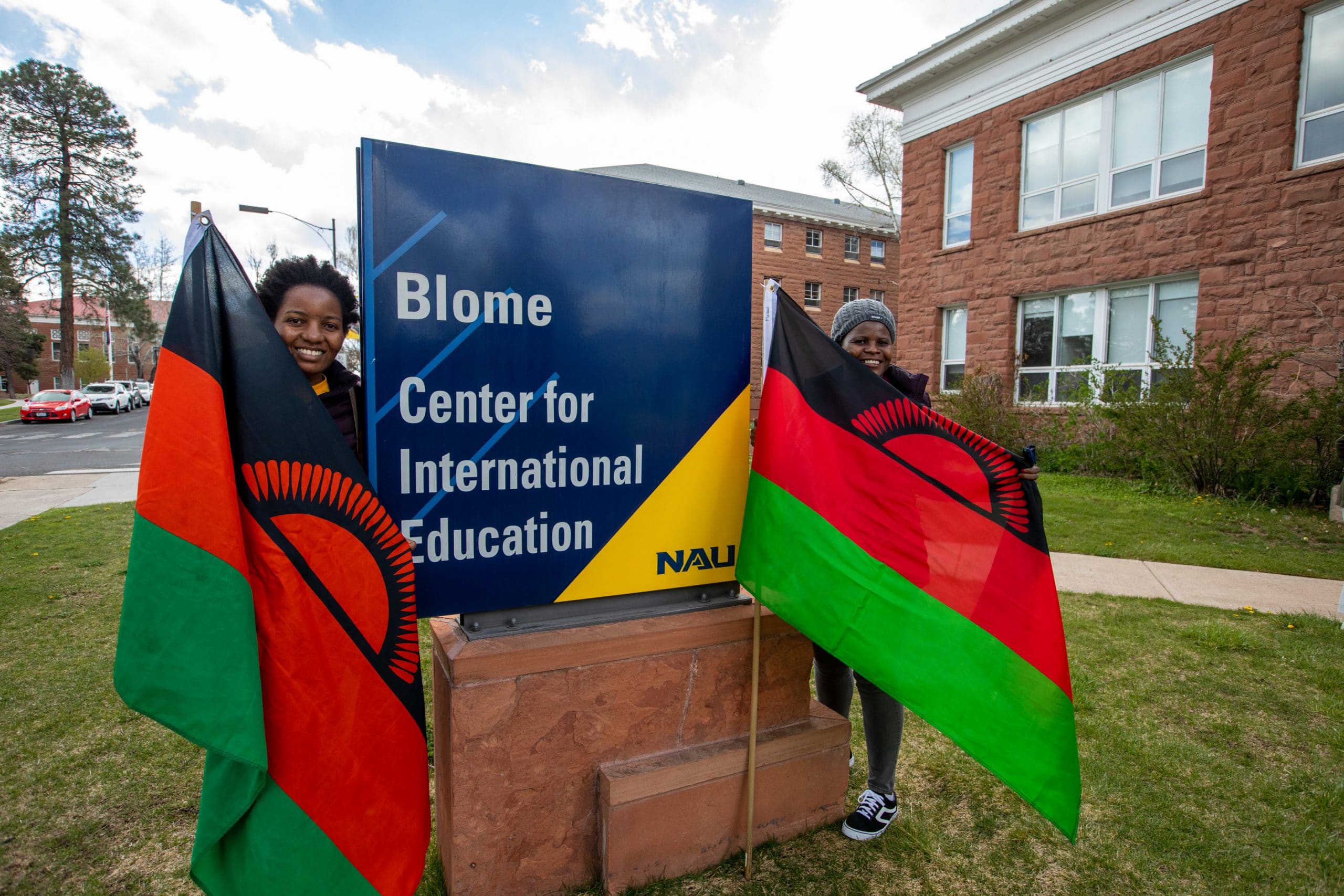 International students stand with flags outside the Blome Center for International Education building.