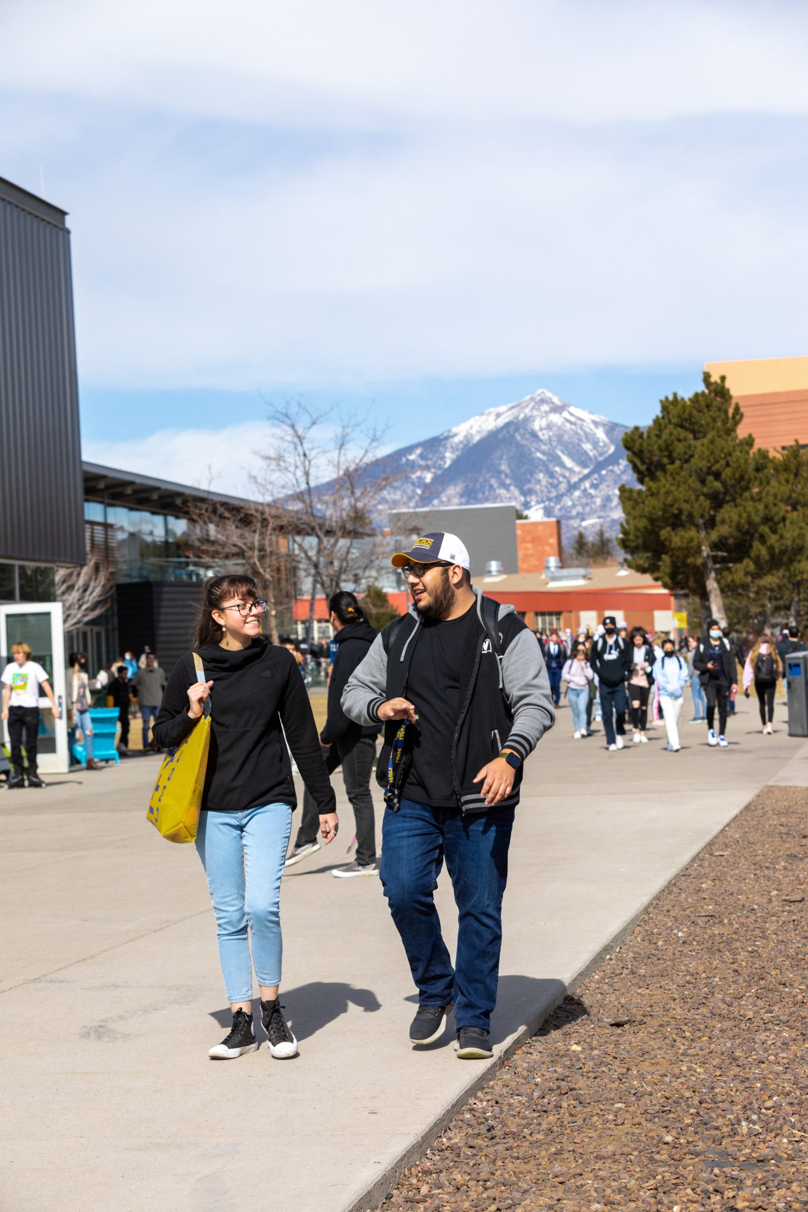 Students walk outside at NAU's Flagstaff campus with the snowcapped peaks in the background.