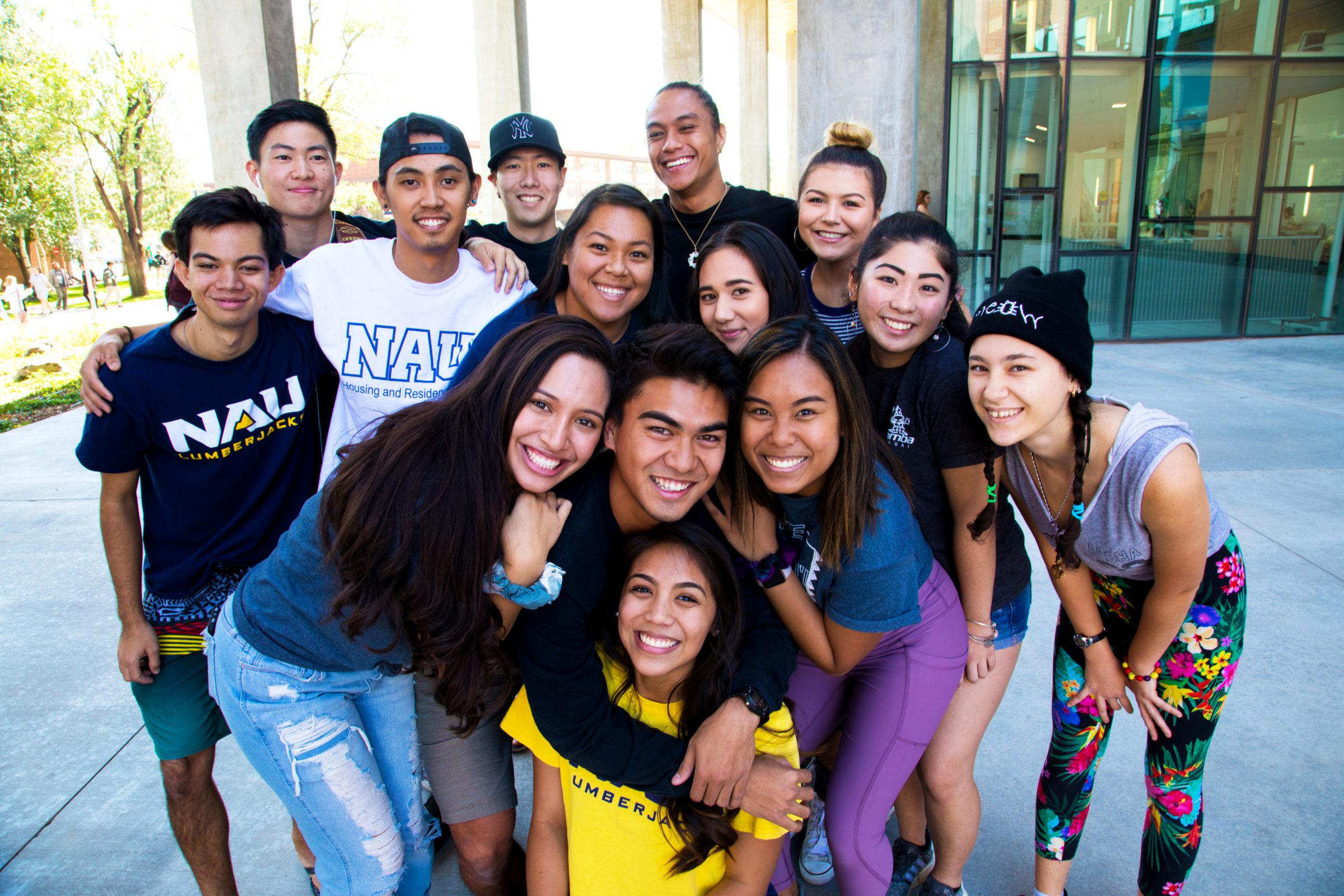 A group of students on campus stand close together, smiling for a picture.