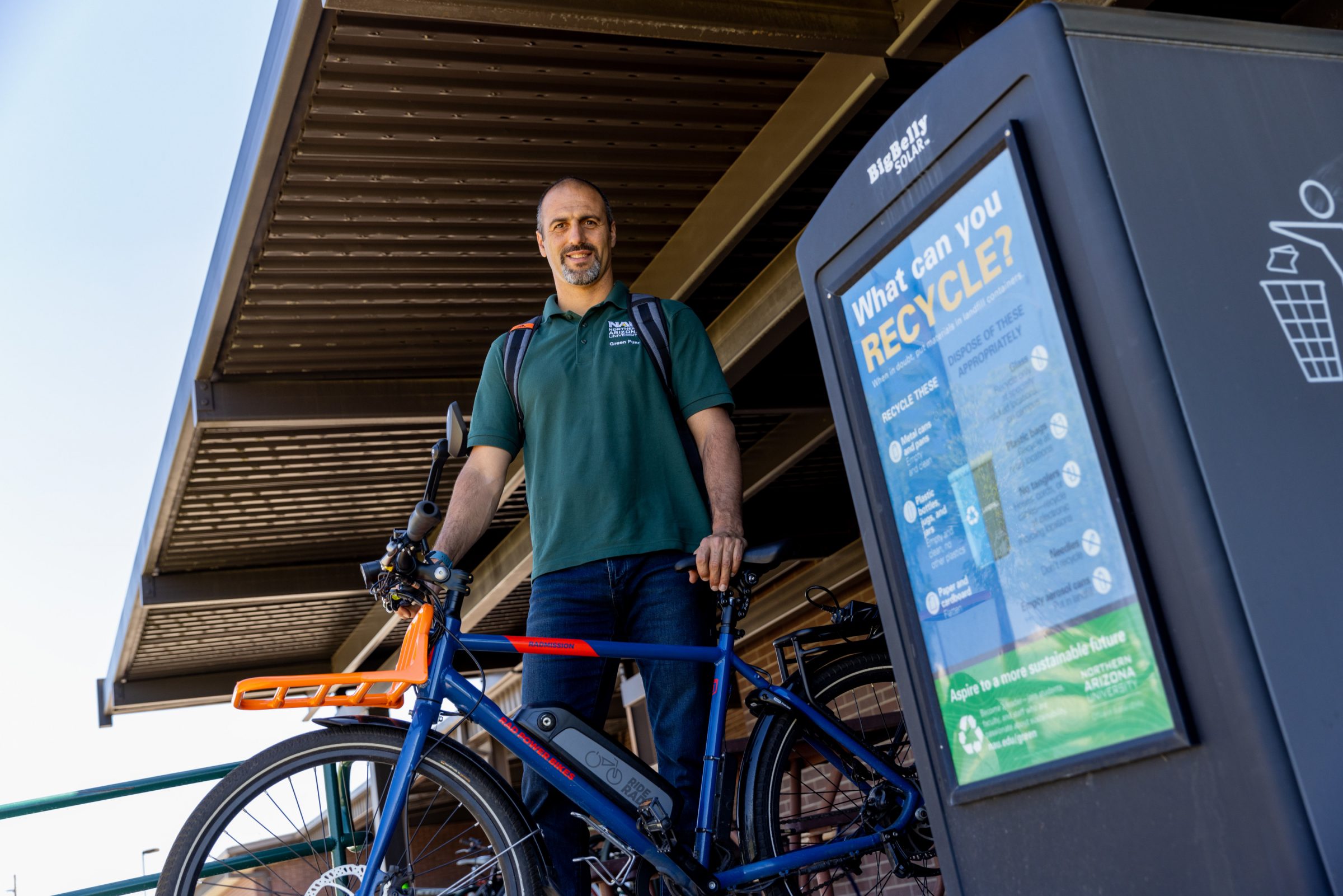 The manager of sustainability, Avi Henn stands by a recycling bin with a bike.