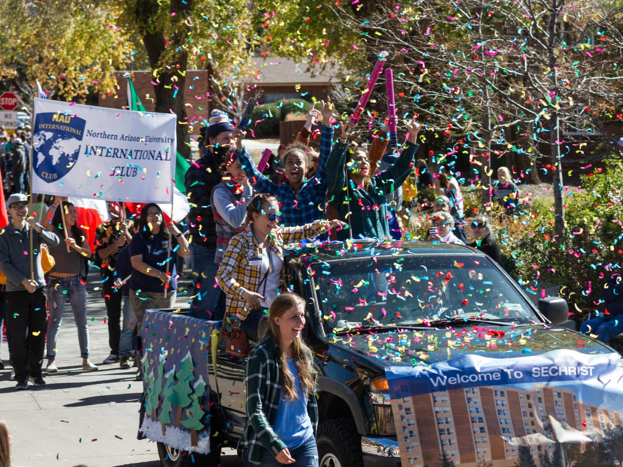 N A U international club smiling and marching the homecoming parade with art work on a truck and confetti everywhere.