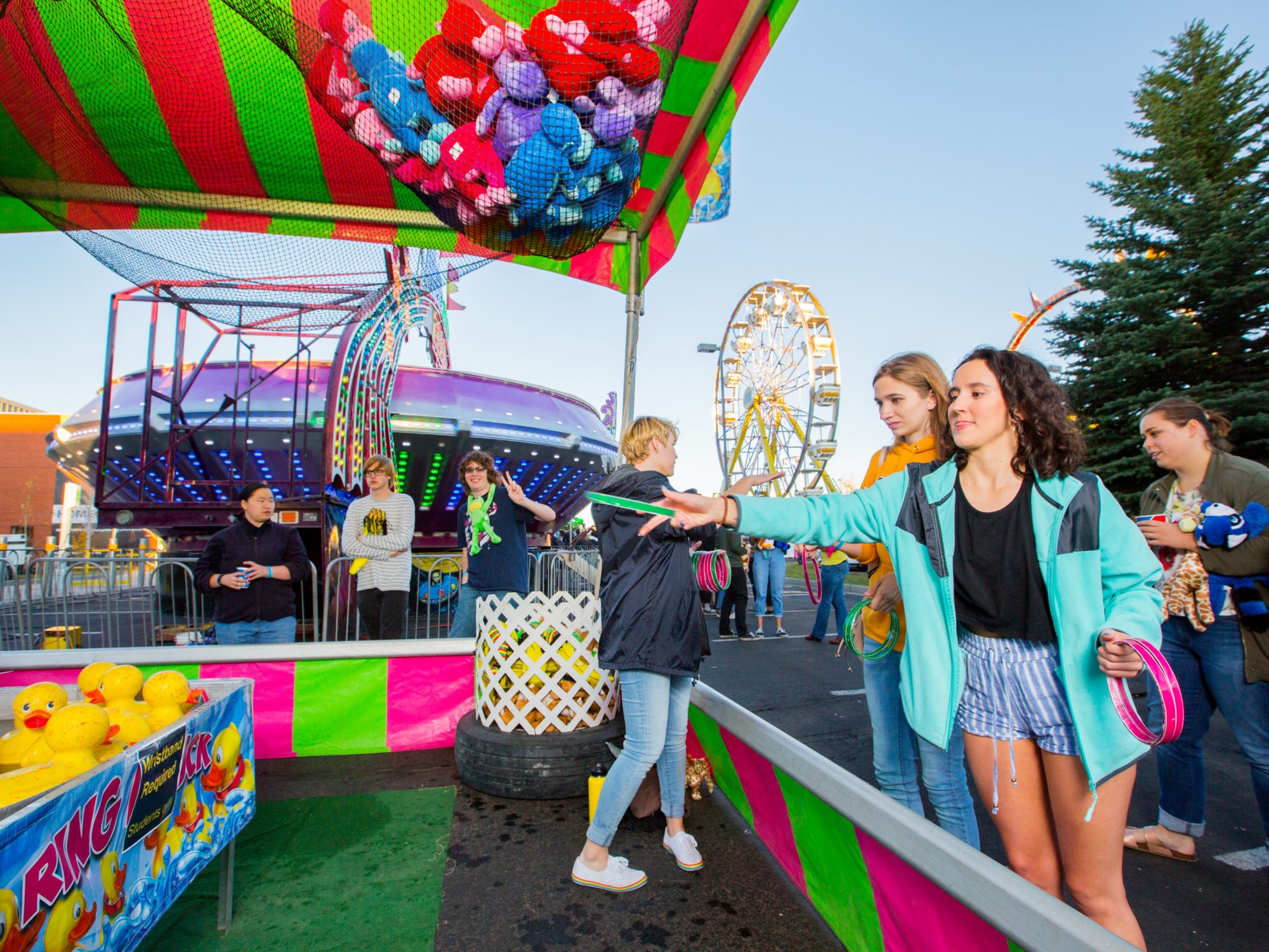N A U students throwing rings in a carnival booth with a student holding a peace sign in the background.