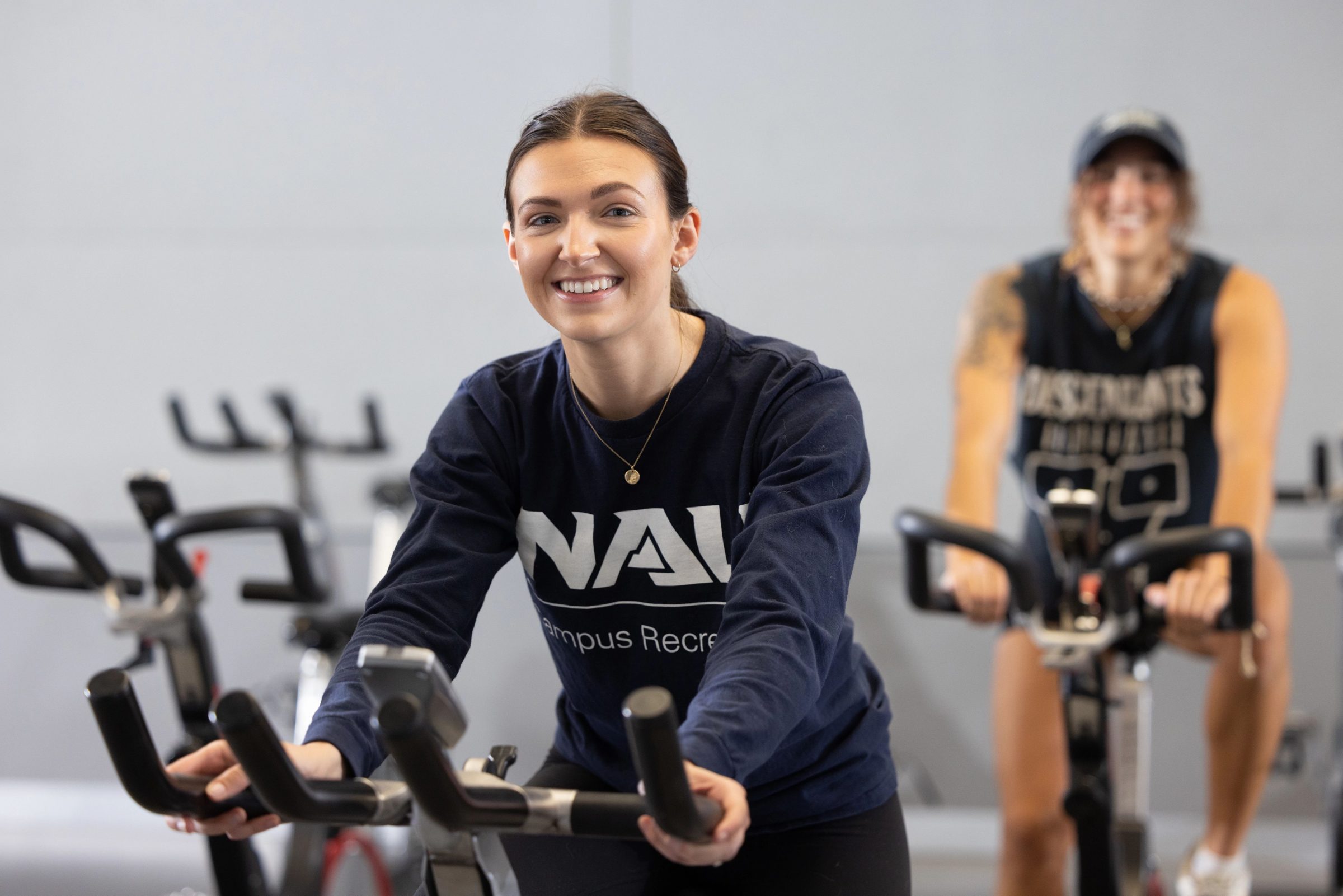 Student using an exercise bike smiling at the camera.