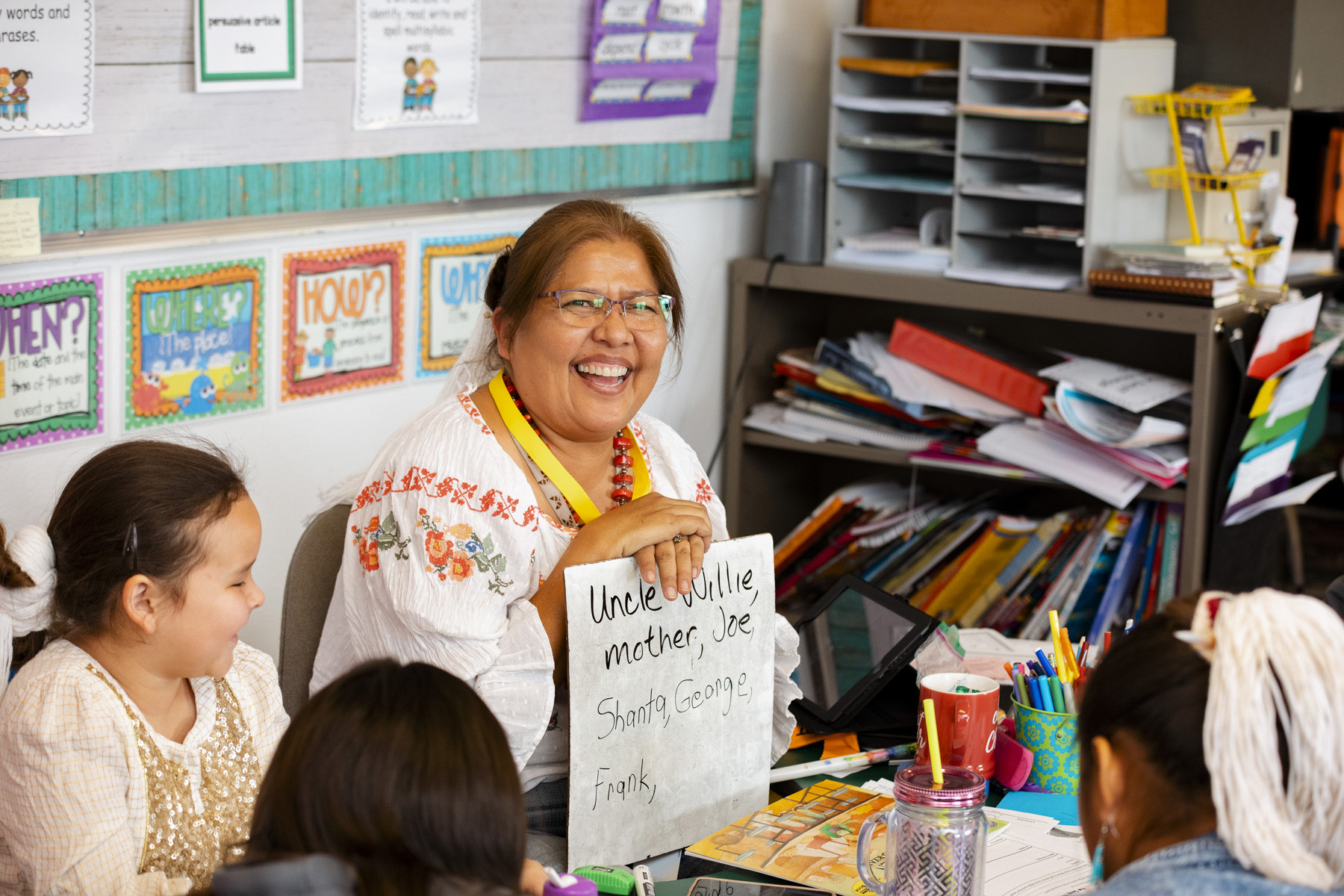 An Indigenous teacher holds up a small whiteboard for her students in a classroom.