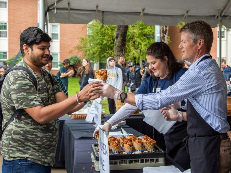 Staff serving food to a student at a barbeque