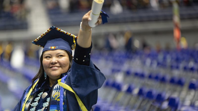 Female student holding diploma up during a commencement ceremony