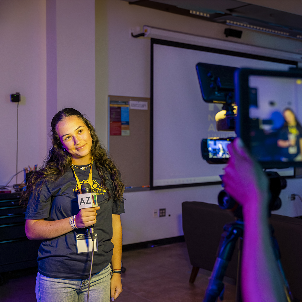 Student stands with a microphone with a camera pointed at them.