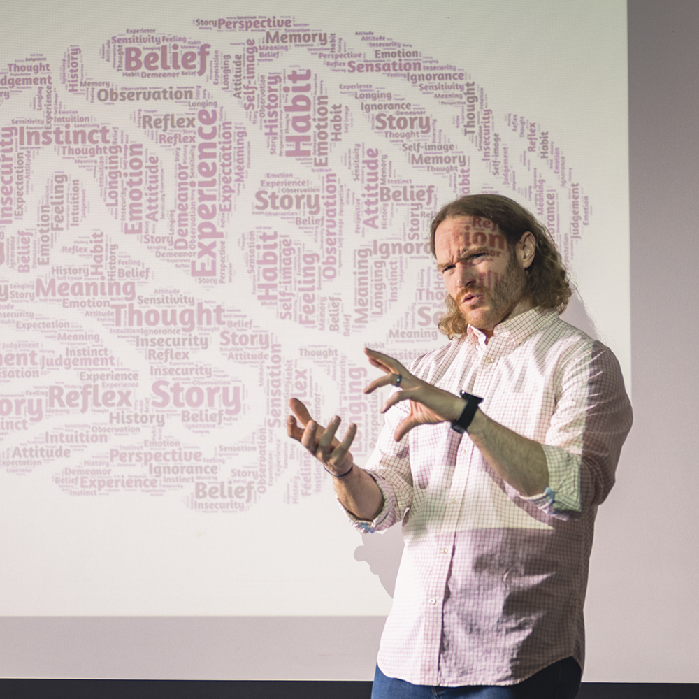 A student giving a presentation while a projector with a brain made of words is on them.