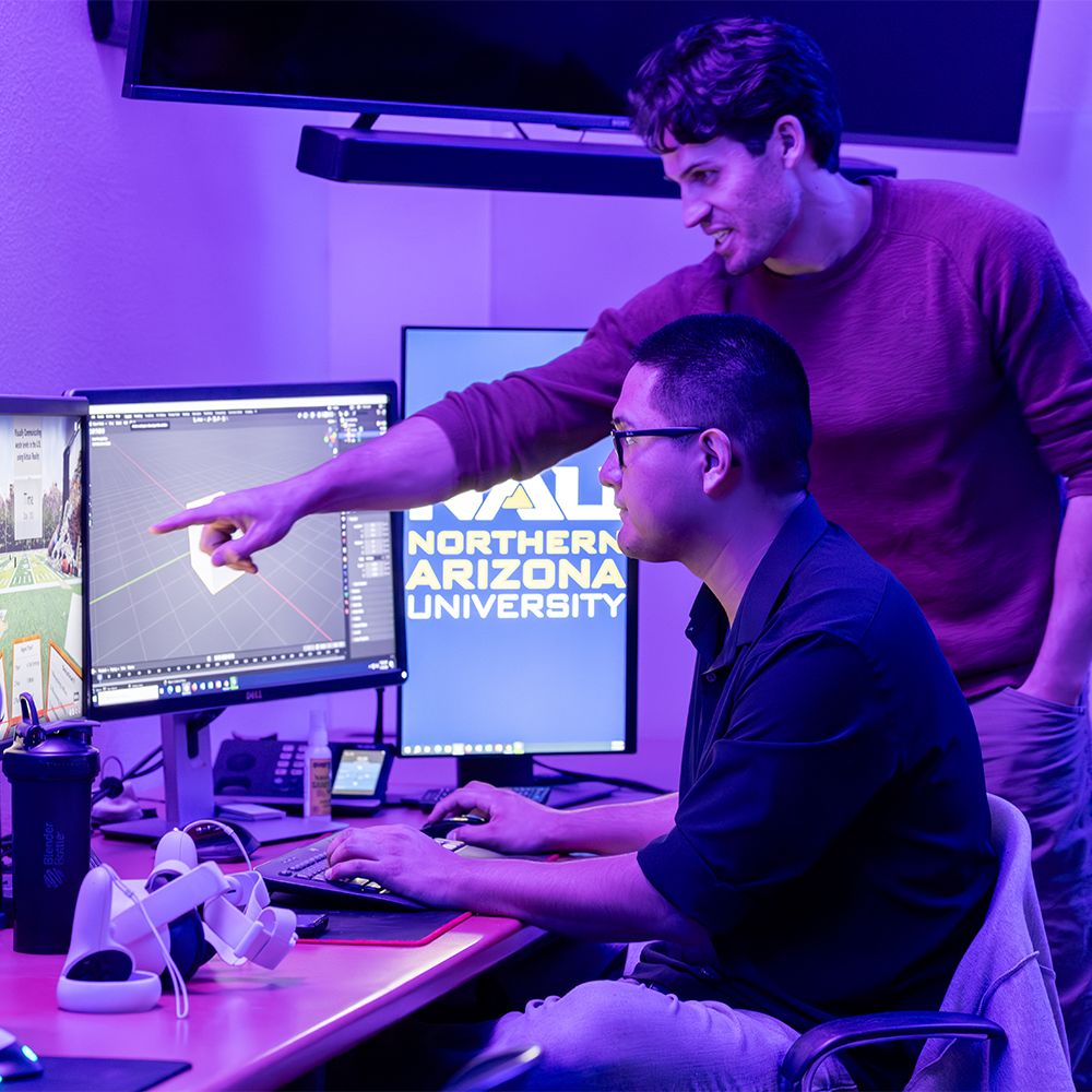 Two students looking at a computer monitor with one pointing at something on the screen.