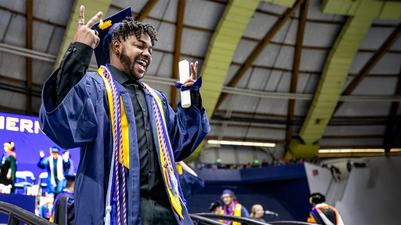 N A U graduate holds up peace signs with their fingers after receiving their diploma.